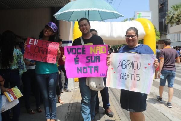 Jovens distribuem abraços em troca de canetas em local de prova.(Imagem:Andrê Nascimento/G1)