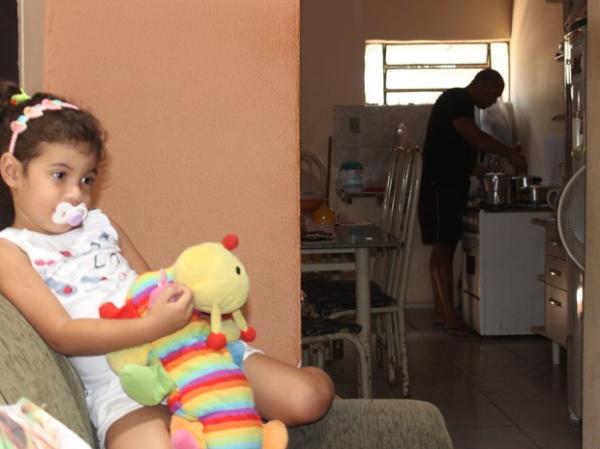 Cledilton faz a comida enquanto a filha assiste TV.(Imagem:Gilcilene Araújo/G1)
