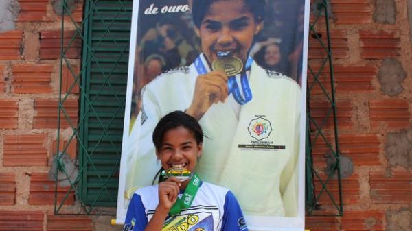 A fama de 'morde medalha' rendeu até um presente inusitado dos colegas de treino: um banner com a foto mordendo a medalha de ouro conquistada nos Jogos Escolares.(Imagem:Náyra Macêdo/GLOBOESPORTE.COM)