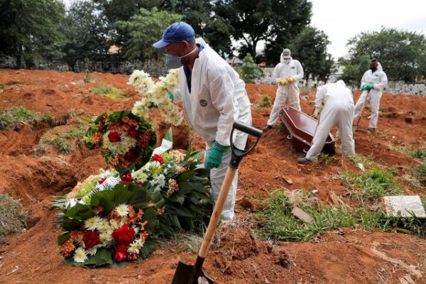 Funcionário de cemitério carrega uma cruz enquanto outros fazem enterro, durante pandemia de coronavírus (Covid-19).(Imagem:Amanda Perobelli/Reuters)